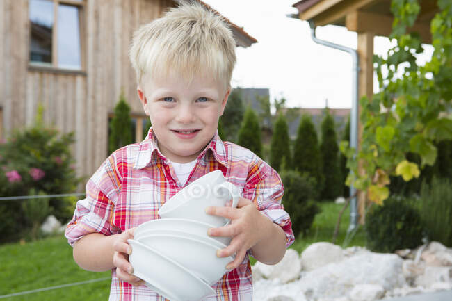 Portrait de garçon dans le jardin portant pile de bols — Photo de stock