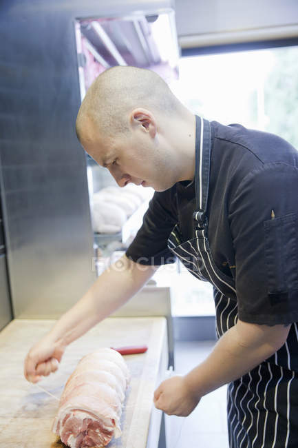 Young butcher tying meat joint in butchers shop — Stock Photo
