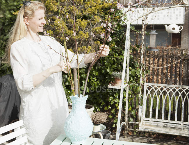 Mitte erwachsene Frau arrangiert Blütenzweige in Vase im Garten — Stockfoto