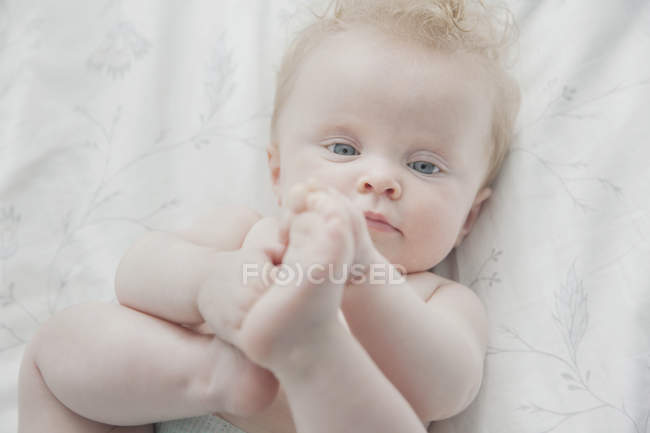 Bambina, sdraiata sul retro, con i piedi in mano — Foto stock