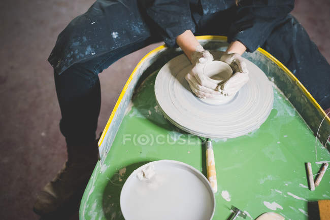 High angle view of young woman, waist down, sitting at pottery wheel making clay pot — Stock Photo