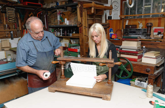Senior man and young woman preparing to bind pages with thread in traditional bookbinding workshop — Stock Photo