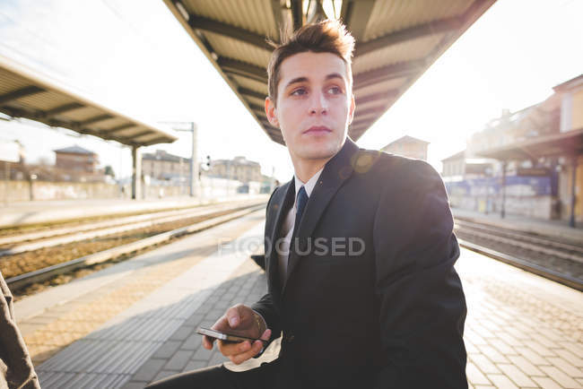 Portrait of young businessman commuter sitting at railway platform. — Stock Photo