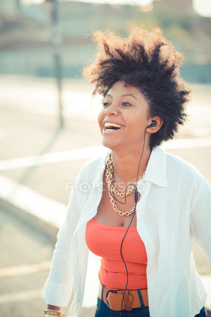 Young woman laughing with music on earphones in city — Stock Photo