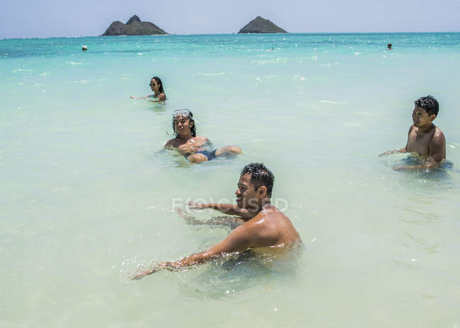 Четверо молодых взрослых друзей играют в море на пляже Ланикай, Оаху, Гавайи, США — стоковое фото