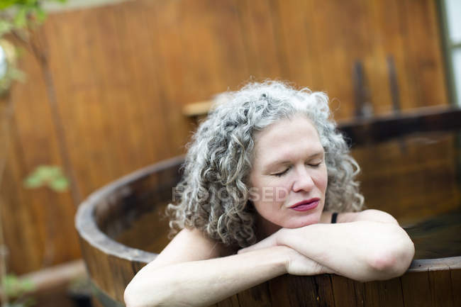 Mature woman resting on hands in hot tub at eco retreat — Stock Photo
