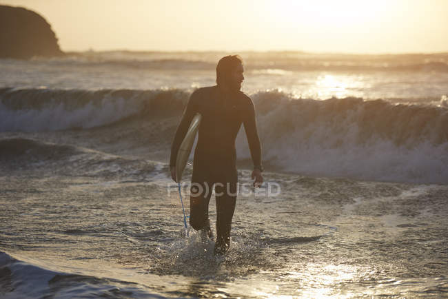 Silhouette of young male surfer carrying surfboard in sea, Devon, England, UK — Stock Photo