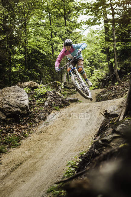 Молода жінка-гірський велосипедистка стрибає середнє повітря в лісі — стокове фото