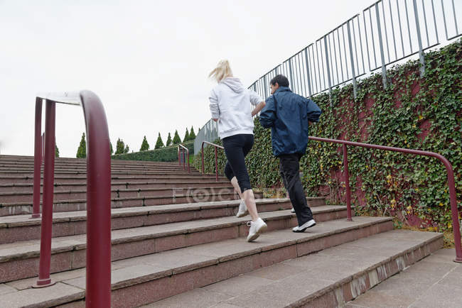 Hombre y mujer corriendo por los escalones juntos, vista trasera - foto de stock