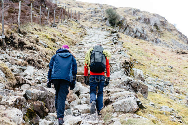 Parejas jóvenes senderismo, vista trasera, Honister Slate Mine, Keswick, Lake District, Cumbria, Reino Unido - foto de stock