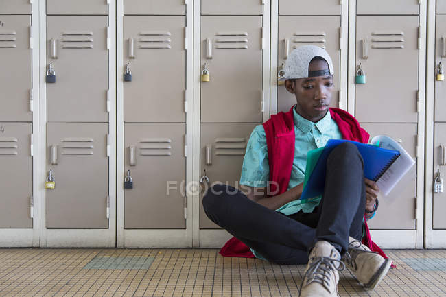 Student leaning against lockers, reading textbook — Stock Photo