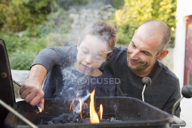 Mid adult man and son lighting barbecue in garden — Stock Photo