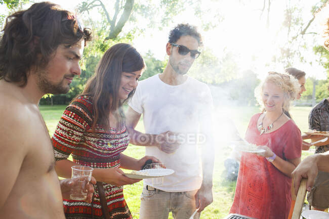 Amigos adultos esperando barbacoa en la fiesta del parque del atardecer - foto de stock