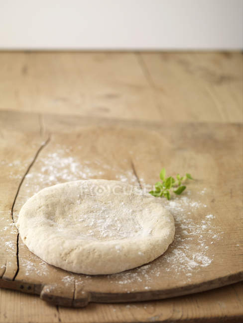 Круг приготовленного теста для пиццы на доске, посыпанной мукой — стоковое фото
