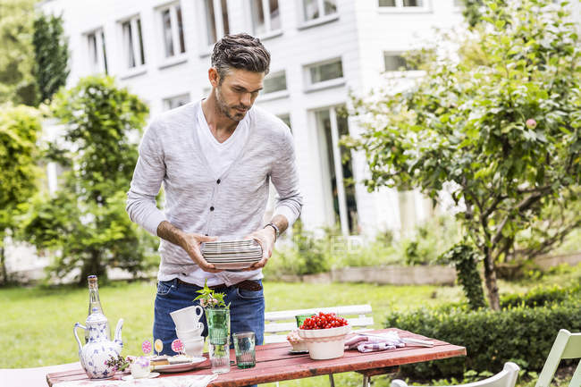 Середній дорослий чоловік в саду, тримає стопки тарілок — стокове фото