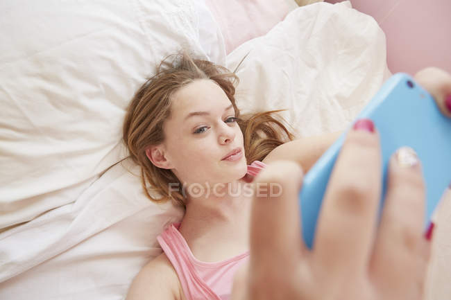 Девушка позирует на кровати для селфи смартфона — стоковое фото