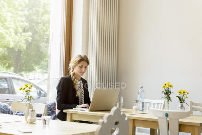 Молода жінка друкує на ноутбуці в кафе — стокове фото