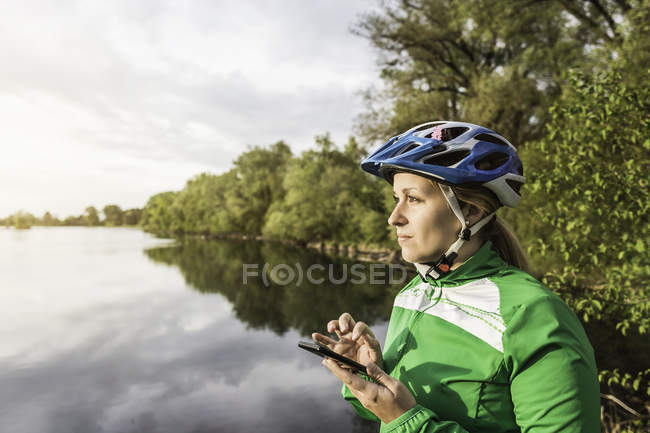Young female at lake texting on smartphone, Augsburg, Bavaria, Germany — Stock Photo