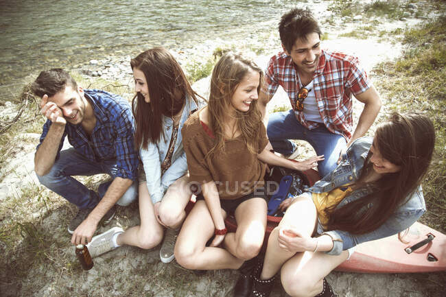 Group of five friends sitting on canoe on riverbank — Stock Photo