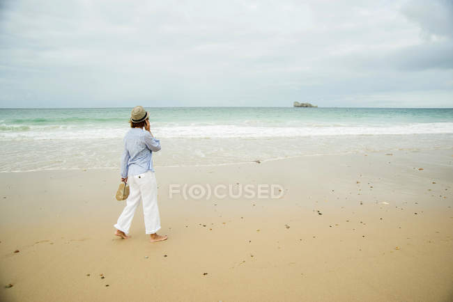 Reife Frau spazieren am Strand plaudert auf Smartphone, Camaret-sur-mer, Bretagne, Frankreich — Stockfoto