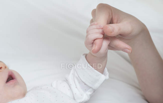 Bébé fille tenant mère doigts sur le lit — Photo de stock