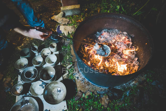 High angle view of young woman using tongs to remove clay pots from fire — Stock Photo