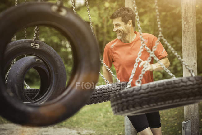 Mature man running by tyre swing looking away smiling — Stock Photo