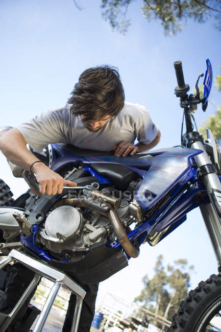 Young male motocross racer adjusting motorcycle engine in forest — Stock Photo