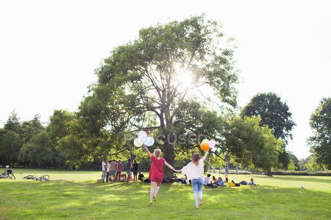 Vista trasera de dos mujeres jóvenes bailando con globos en la fiesta del parque - foto de stock