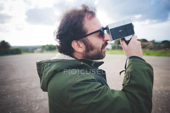 Mid adult man using vintage movie camera on waste ground — Stock Photo