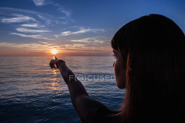 Silhouetted young woman pointing at sunset from beach, Oristano, Sardinia, Italy — Stock Photo