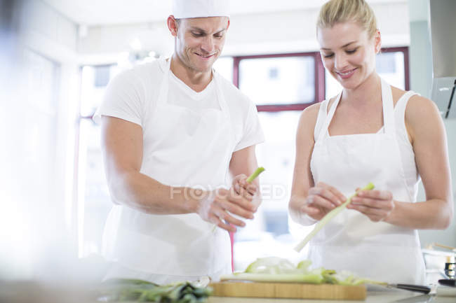 Chefs machos y hembras pelando puerros en cocina comercial - foto de stock
