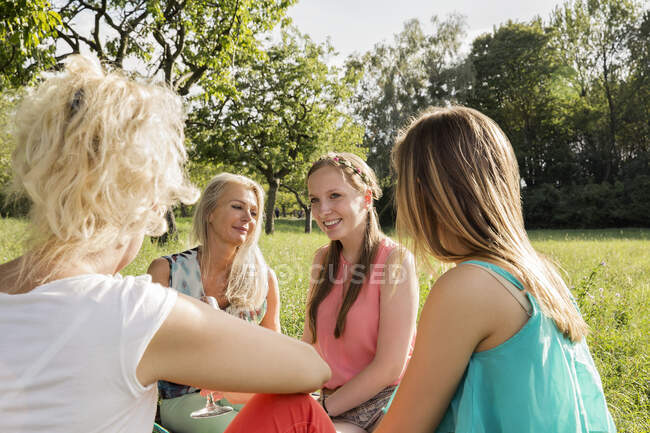 Женщины сидят в парке, пьют вино, разговаривают и улыбаются. — стоковое фото