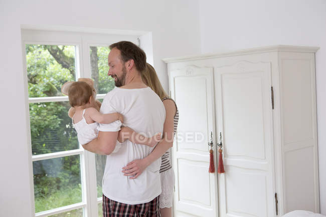 Padre sosteniendo hija bebé, mujer con brazo alrededor del hombre - foto de stock