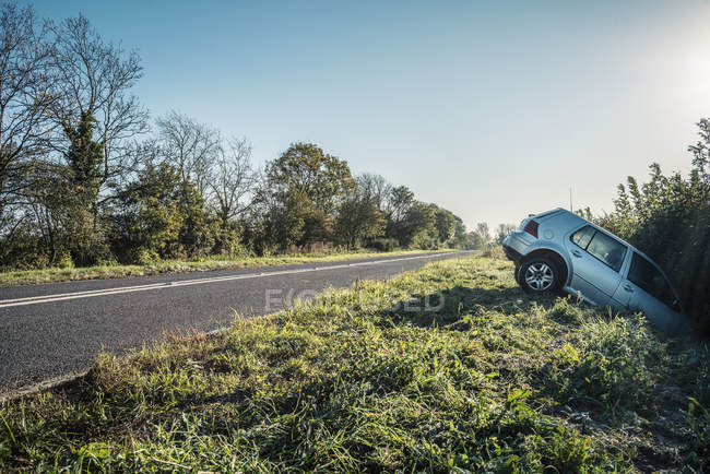 Разбившийся автомобиль, торчащий из изгороди на сельской дороге — стоковое фото