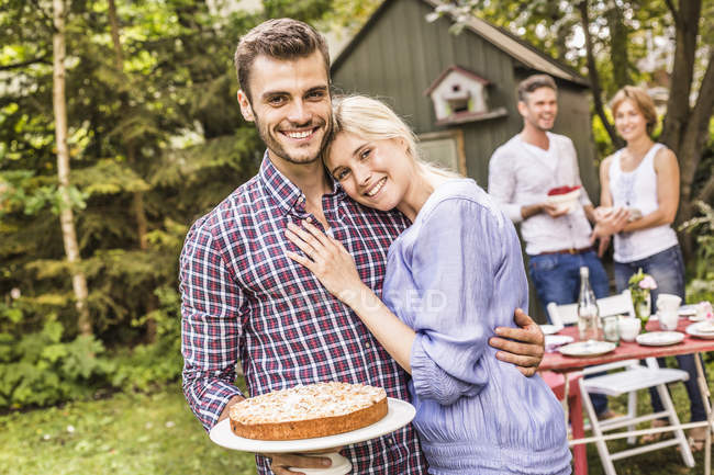 Group of friends at garden party, young man holding cake — Stock Photo