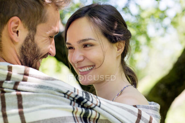 Cabeza y hombros de pareja joven envueltos en manta cara a cara sonriendo - foto de stock
