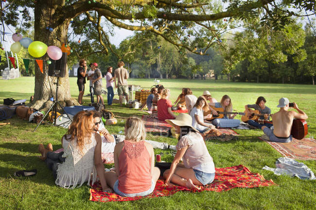 Група друзів, які слухають музику під парковим деревом на вечірці заходу сонця — стокове фото