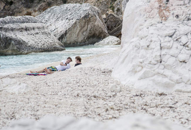 Jovens relaxantes na praia rochosa usando smartphone, Golfo di Orosei, Sardenha, Itália — Fotografia de Stock