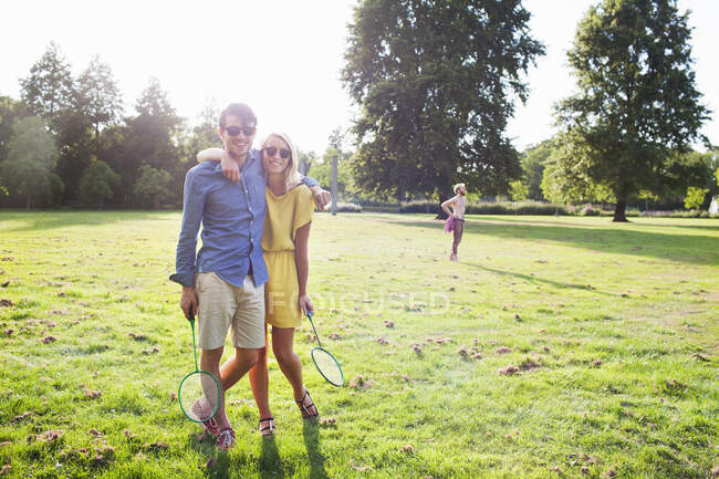 Casal jovem romântico com raquetes de badminton no parque iluminado pelo sol — Fotografia de Stock
