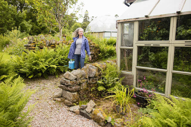 Mujer madura llevando regadera en el jardín - foto de stock