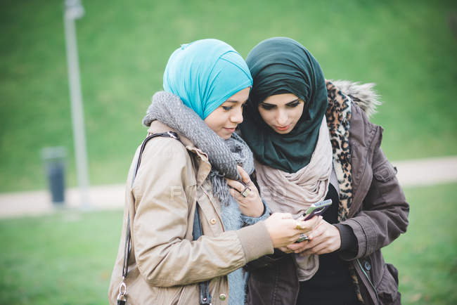 Dos amigas en el parque leyendo texto en smartphones - foto de stock