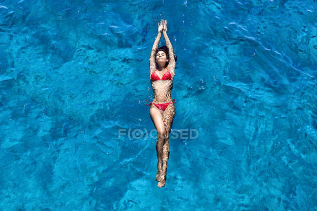 Mulher nova em biquíni vermelho flutuando na água do mar azul, ângulo alto — Fotografia de Stock