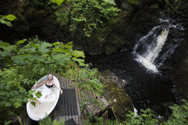 Вид под высоким углом на зрелую женщину в ванне с мыльным пузырем перед водопадом во время эколечения — стоковое фото