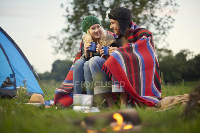 Jeune couple de camping assis près du feu de camp avec une tasse de thé — Photo de stock