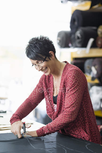 Costureira madura usando tesouras para cortar têxteis na mesa de trabalho — Fotografia de Stock