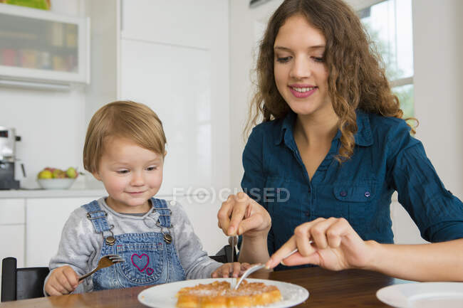 Teenage girl cutting cake for female toddler at kitchen table — Stock Photo