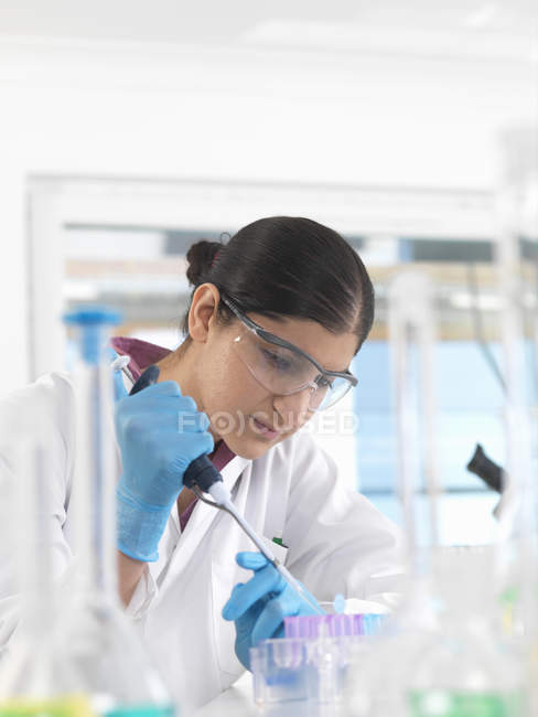 Muestra de mujer joven científica pipeteando en un vial en un laboratorio utilizado para pruebas químicas y de ADN - foto de stock