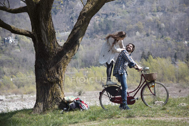 Молода жінка стоїть на велосипеді за хлопцем — стокове фото