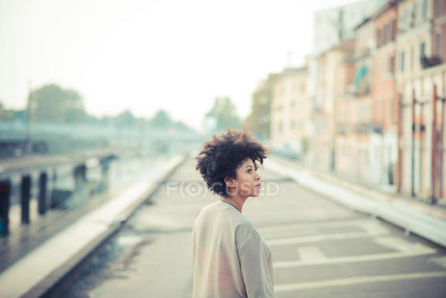 Jovem mulher olhando por cima do ombro na cidade — Fotografia de Stock